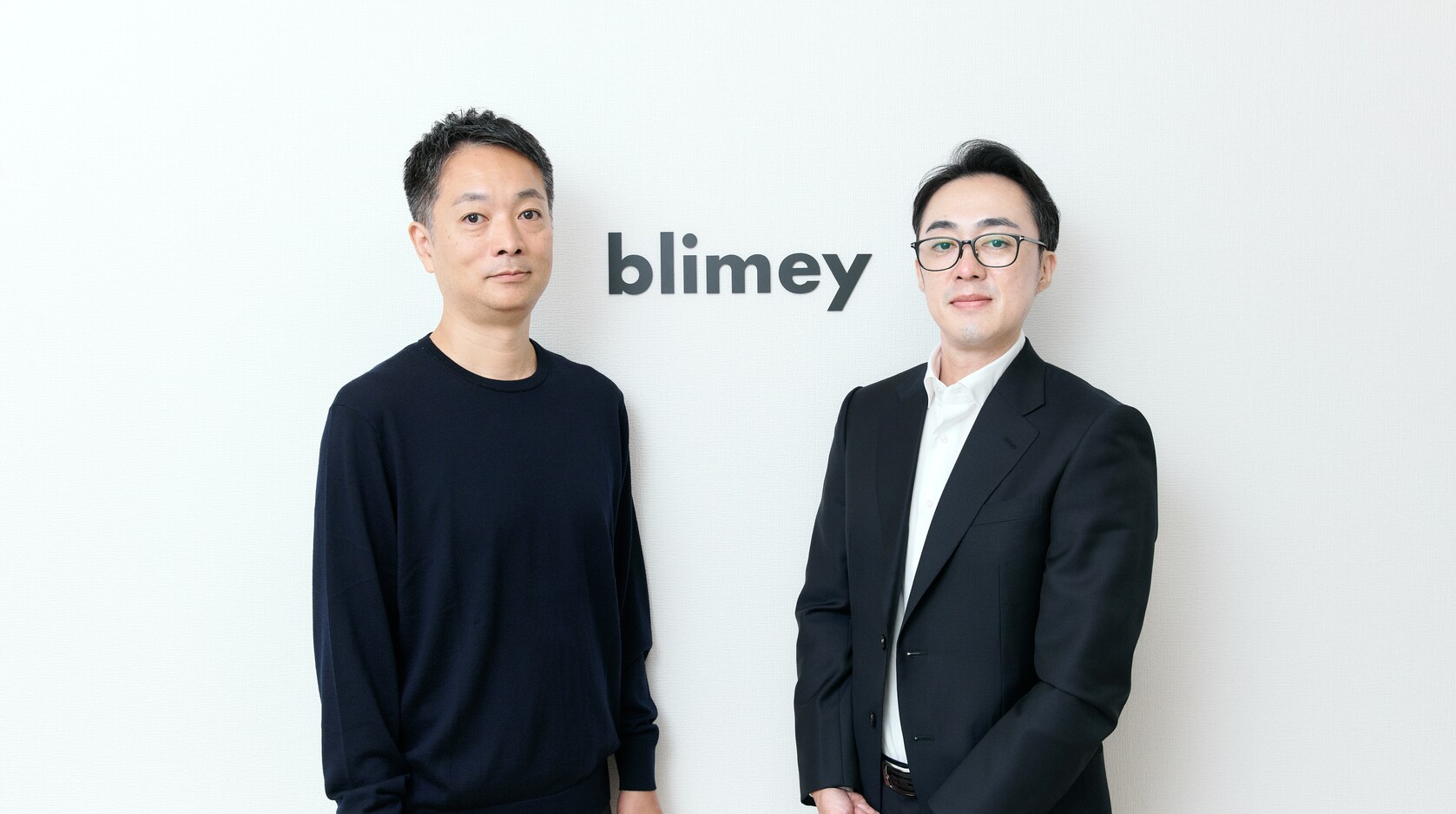 blimeyのロゴ前に立つ代表と取締役